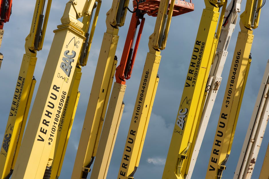 Multiple yellow boom lifts with text and numbers arranged against a blue sky.